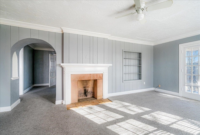 Unfurnished living room featuring carpet floors, crown molding, a textured ceiling, arched walkways, and built in features