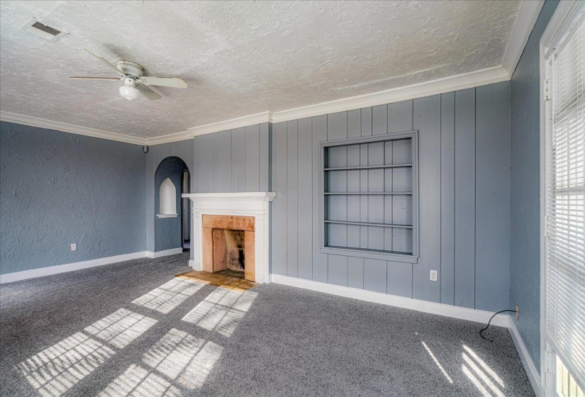 Unfurnished living room with ornamental molding, built in shelves, a fireplace with flush hearth, carpet flooring, and a textured ceiling