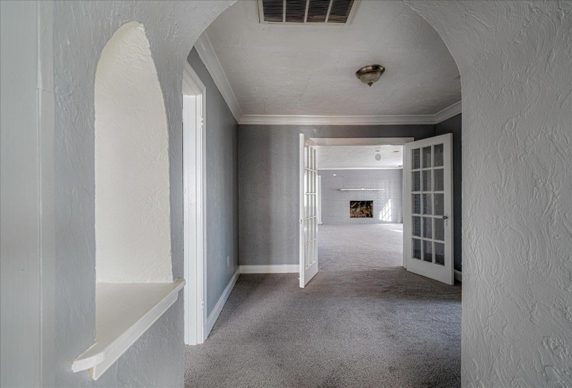 Corridor featuring a textured wall, carpet flooring, french doors, arched walkways, and ornamental molding