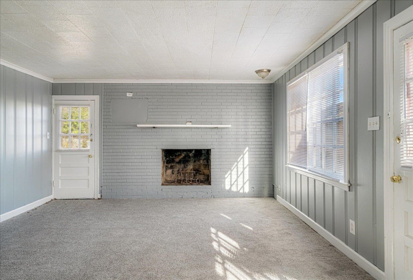 Unfurnished living room with a brick fireplace, wooden walls, carpet flooring, and ornamental molding