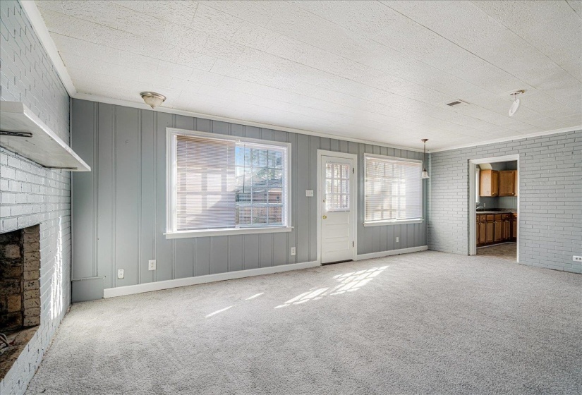 Unfurnished living room featuring brick wall, carpet flooring, and a brick fireplace