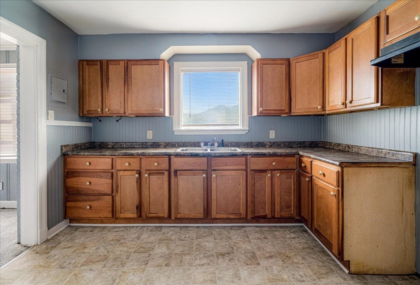 Kitchen featuring dark countertops, brown cabinetry, ventilation hood, wood walls, and electric panel