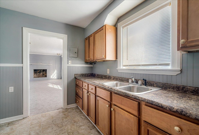 Kitchen with dark countertops, a fireplace, brown cabinetry, wainscoting, and wood walls