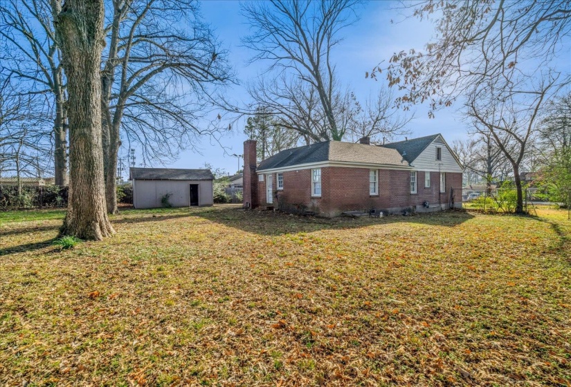 View of side of property with brick siding, an outbuilding, a lawn, and a chimney