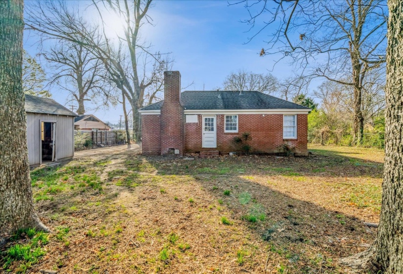 Rear view of house with brick siding, a chimney, an outbuilding, and a shingled roof