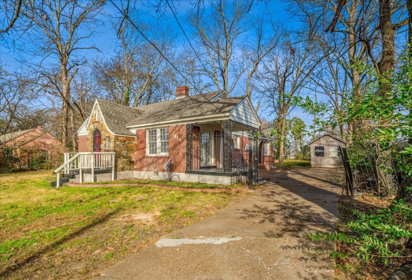 View of front of house with an outdoor structure, brick siding, a chimney, driveway, and a front lawn