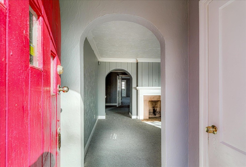 Hallway with a textured wall, arched walkways, crown molding, and a textured ceiling