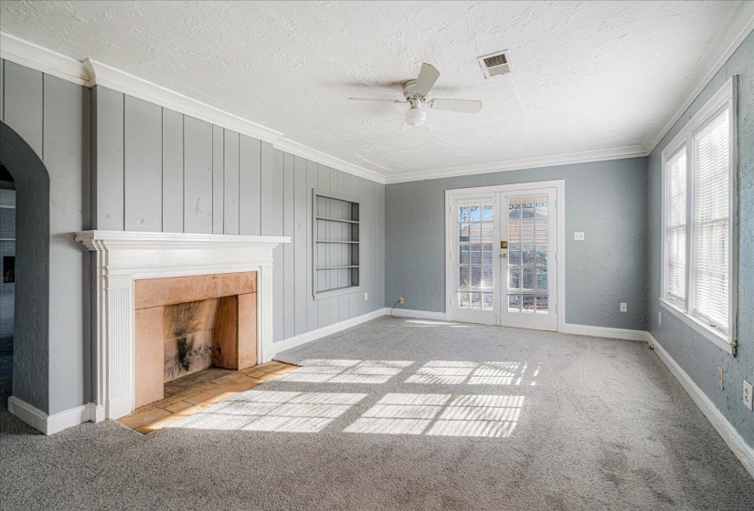 Unfurnished living room featuring ornamental molding, carpet floors, built in shelves, a textured ceiling, and a tile fireplace