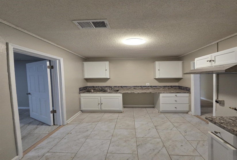 Kitchen with a textured ceiling, white cabinets, dark stone countertops, light marble finish flooring, and crown molding