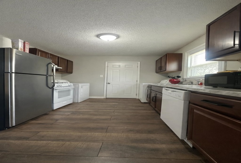 Kitchen featuring white appliances, a textured ceiling, dark wood-type flooring, dark wood finish cabinets, and light countertops