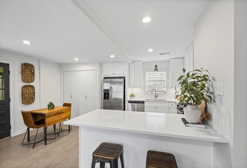 Kitchen with a peninsula, a kitchen bar, white cabinets, light stone countertops, and recessed lighting