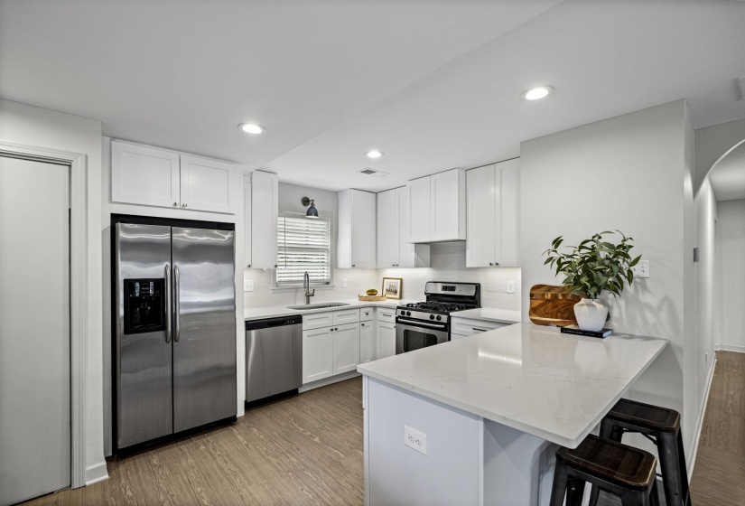 Kitchen with a peninsula, stainless steel appliances, white cabinets, dark wood-type flooring, and a breakfast bar