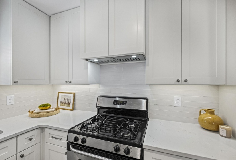 Kitchen featuring stainless steel gas range oven, white cabinets, and light stone counters
