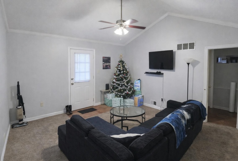 Carpeted living room featuring a ceiling fan and crown molding