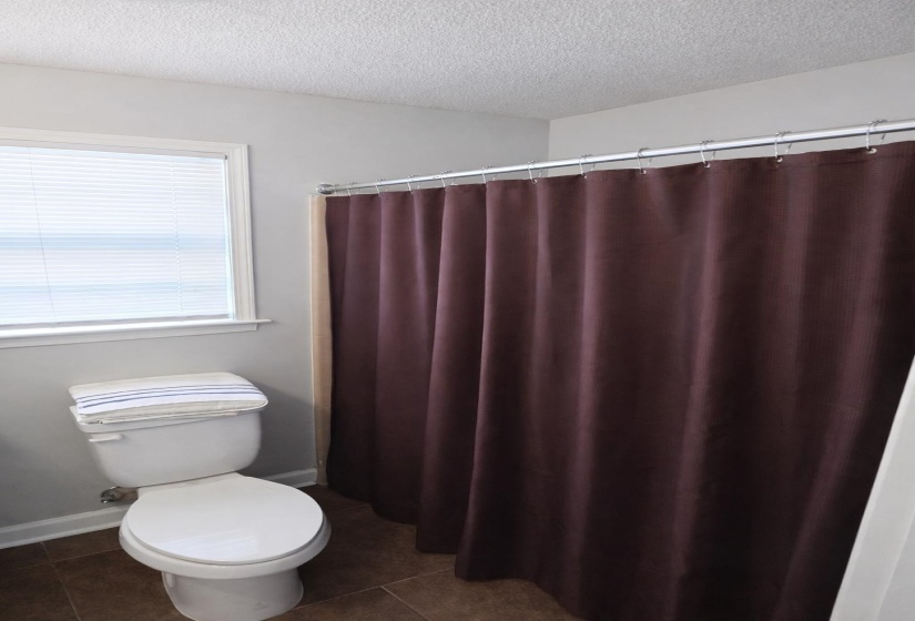 Full bathroom featuring a textured ceiling, curtained shower, and dark tile patterned floors