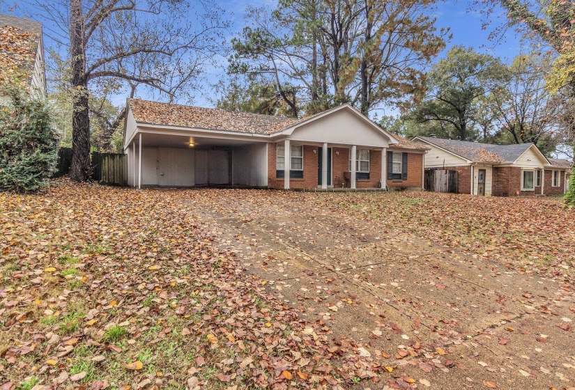 Single story home with a porch, driveway, brick siding, and a carport