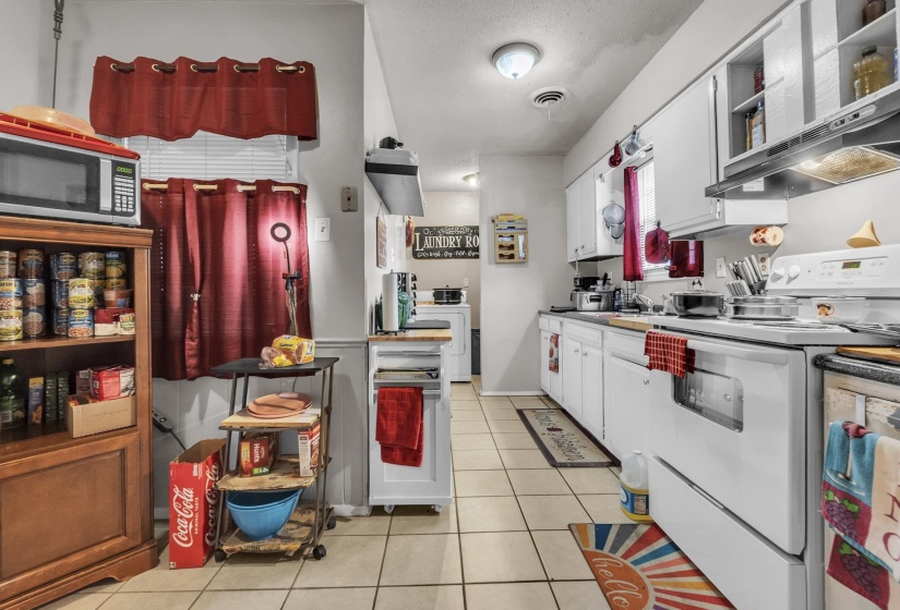 Kitchen with white electric stove, white cabinets, light tile patterned flooring, stainless steel microwave, and open shelves