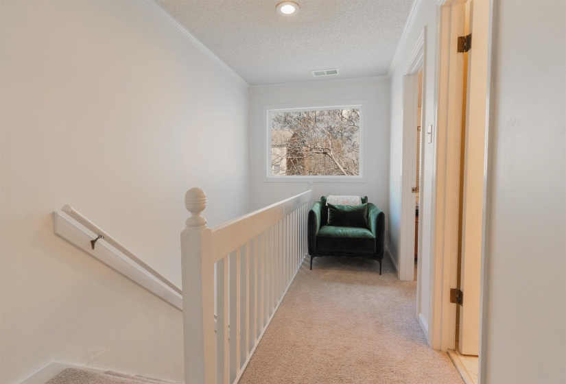 Corridor featuring light colored carpet, an upstairs landing, and a textured ceiling
