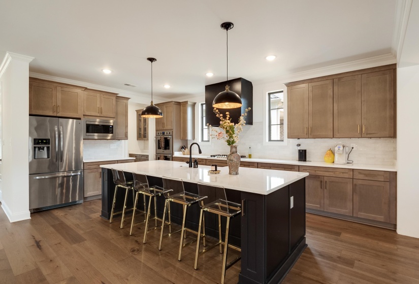 Dual tone kitchen with tasteful backsplash, stainless steel appliances, a kitchen breakfast bar, crown molding, and a center island with sink