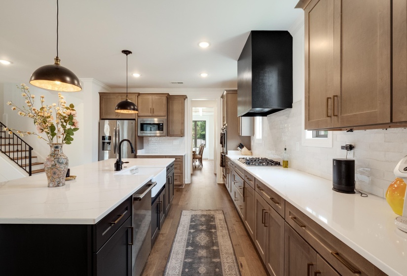 Kitchen with dark wood-style floors, a center island with sink, hanging light fixtures, stainless steel appliances, and ornamental molding