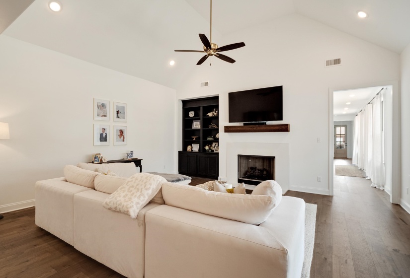 Living room with recessed lighting, dark wood-type flooring, built in shelves, a fireplace, and ceiling fan