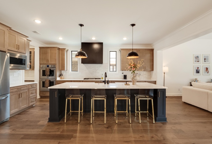 Two tone kitchen with ornamental molding, a kitchen bar, dark wood-style flooring, stainless steel appliances, and a spacious island