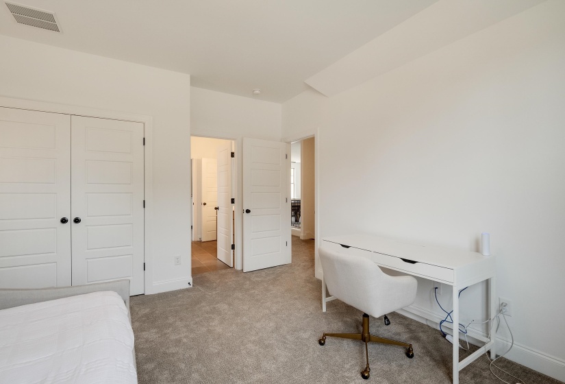 Bedroom with a closet, light carpet, and a desk