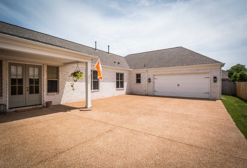 Rear view of property featuring an attached garage, roof with shingles, brick siding, concrete driveway, and a patio