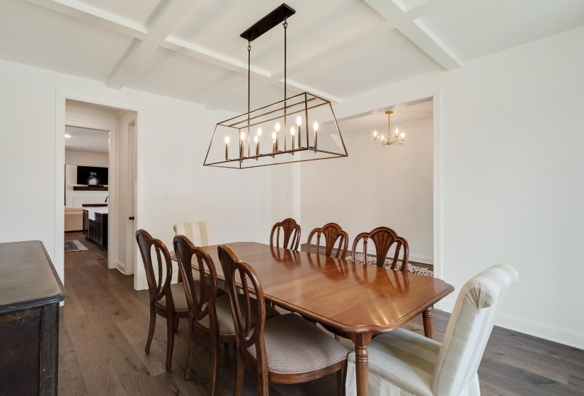 Dining area with coffered ceiling, dark wood-style floors, a chandelier, and a fireplace
