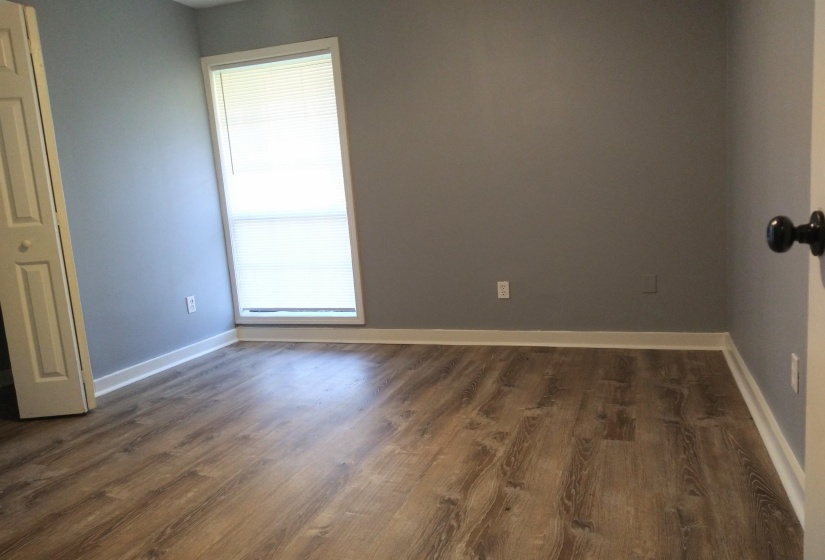 Primary bedroom with dark wood finished floors, double door closet, and baseboards.