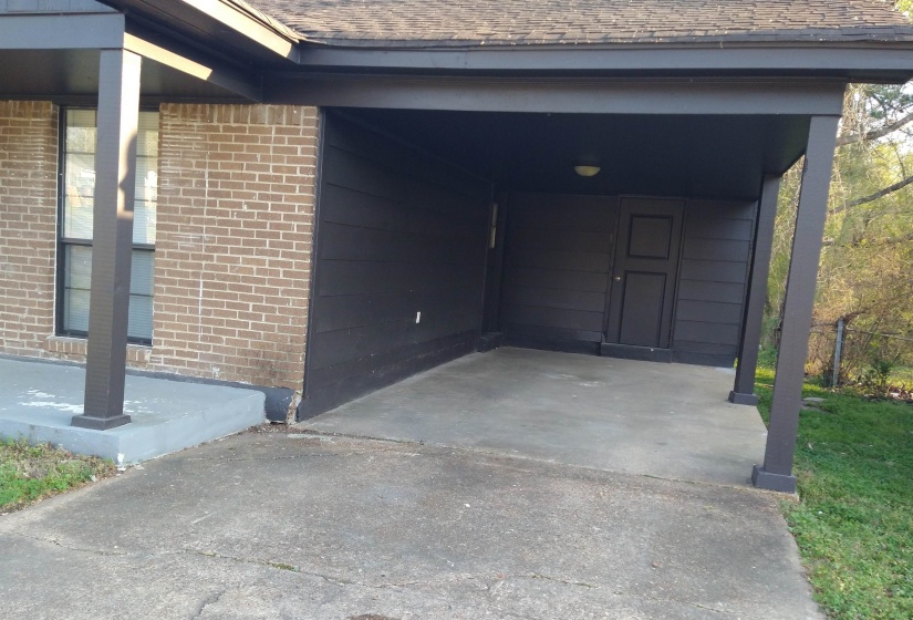 View of Carport with door to storage room and side entrance into Kitchen.