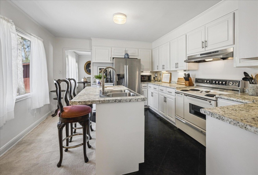 Kitchen featuring range with two ovens, light countertops, a center island with sink, white cabinets, and ornamental molding