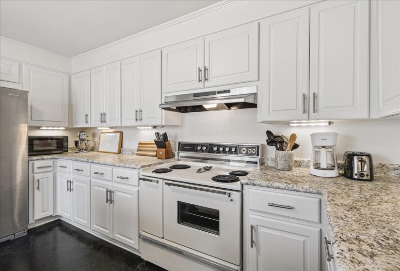 Kitchen with electric stove, freestanding refrigerator, white cabinets, light stone counters, and black microwave