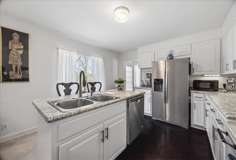 Kitchen with white cabinets, stainless steel appliances, light countertops, and a kitchen island with sink