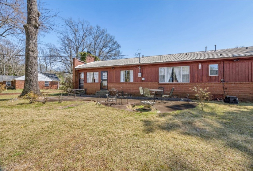 Back of house with a patio, a chimney, a lawn, and a metal roof