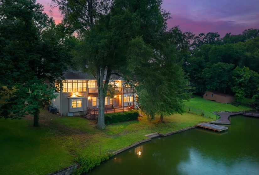 Back of property at dusk with a yard, a deck with water view, and view of scattered trees
