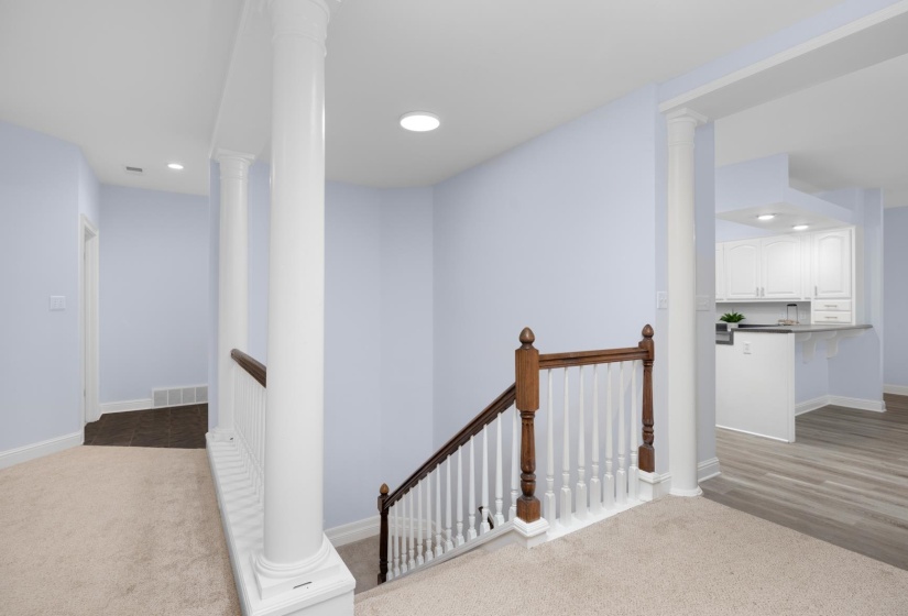 Hall with light colored carpet, an upstairs landing, recessed lighting, and ornate columns