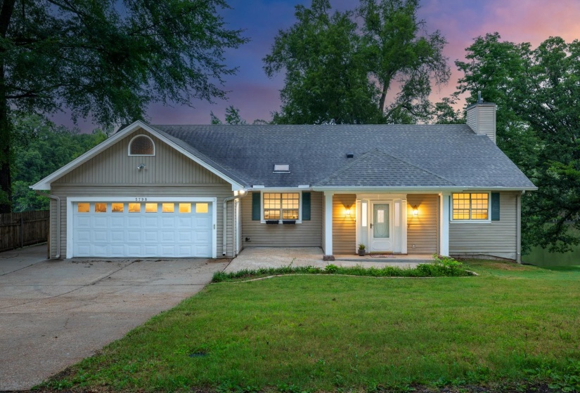 Single story home with a porch, concrete driveway, roof with shingles, and a lawn