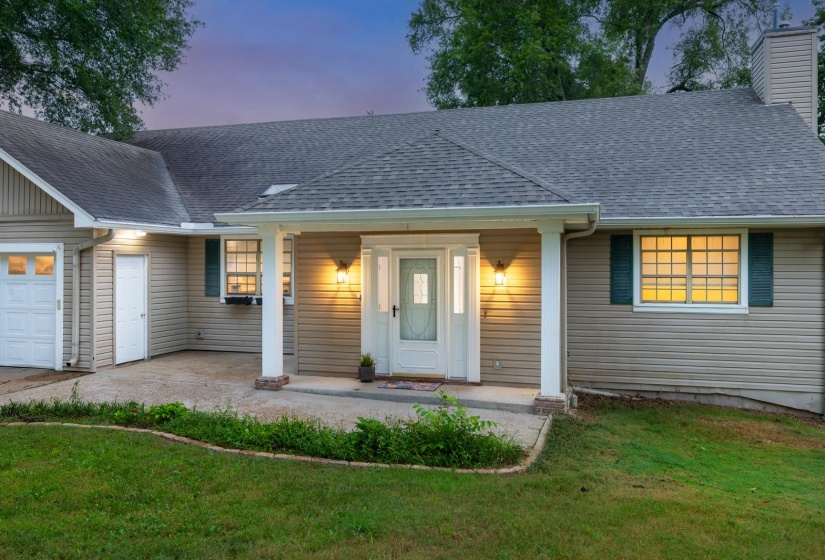 View of front of home featuring a lawn, a garage, a shingled roof, a chimney, and covered porch