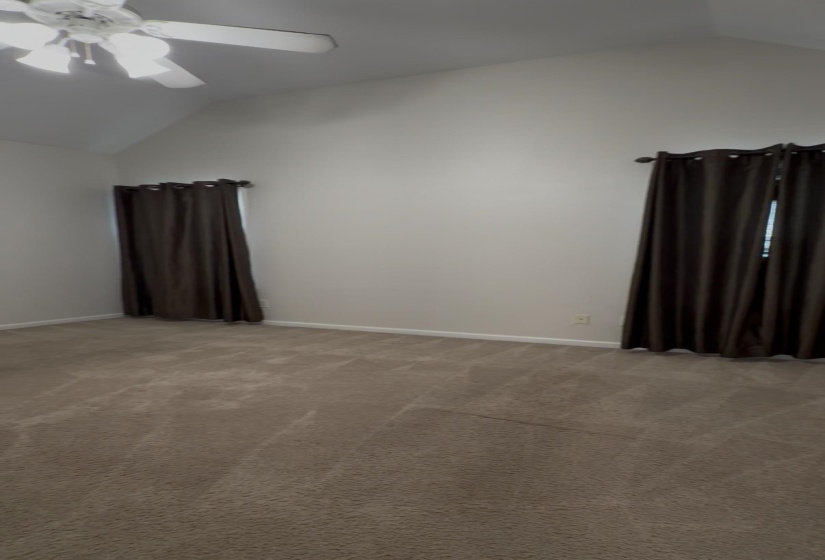 Vaulted ceiling room with neutral carpet flooring and a ceiling fan fixture