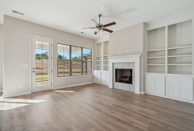 Unfurnished living room featuring built in shelves, ceiling fan, light wood finished floors, and a fireplace