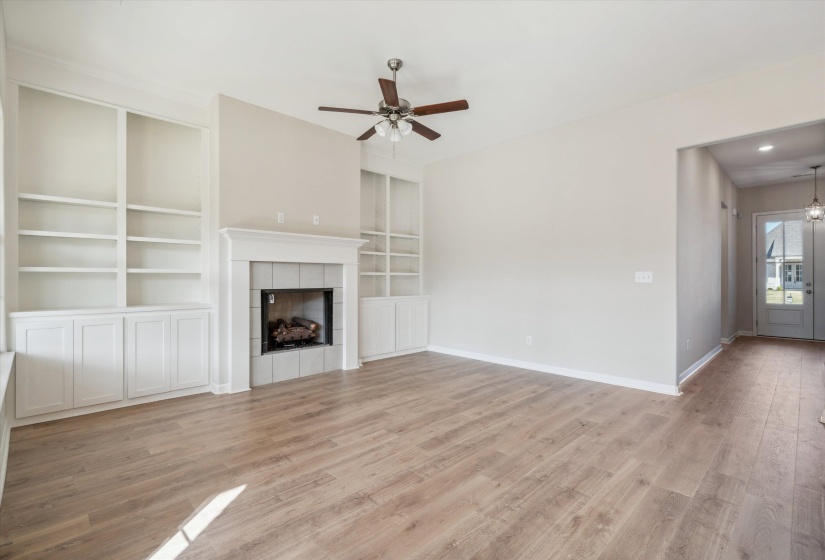 Unfurnished living room featuring built in features, ceiling fan, light wood-style floors, and a fireplace