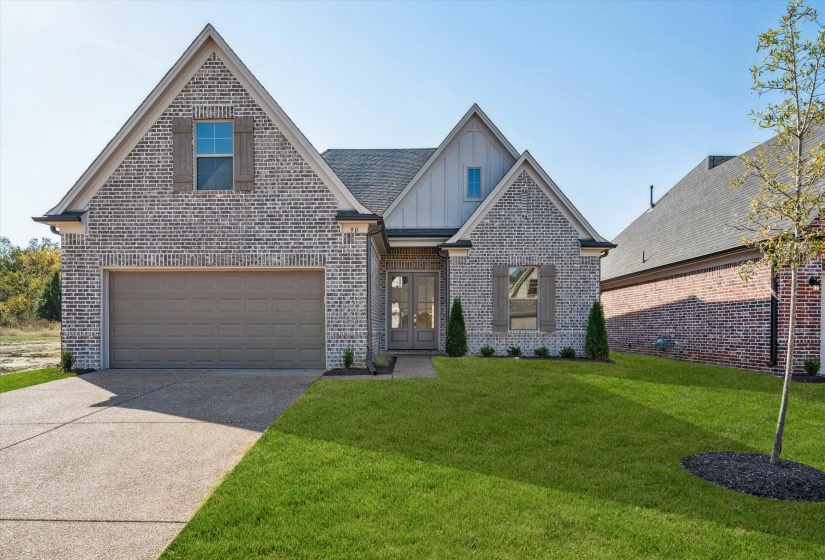 View of front of home with board and batten siding, a front lawn, brick siding, concrete driveway, and french doors