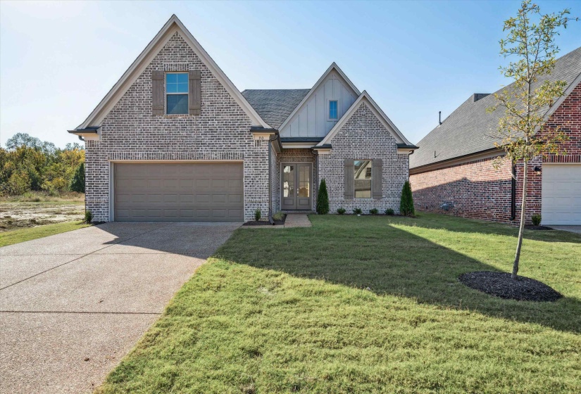 View of front of home featuring brick siding, a front yard, board and batten siding, and concrete driveway