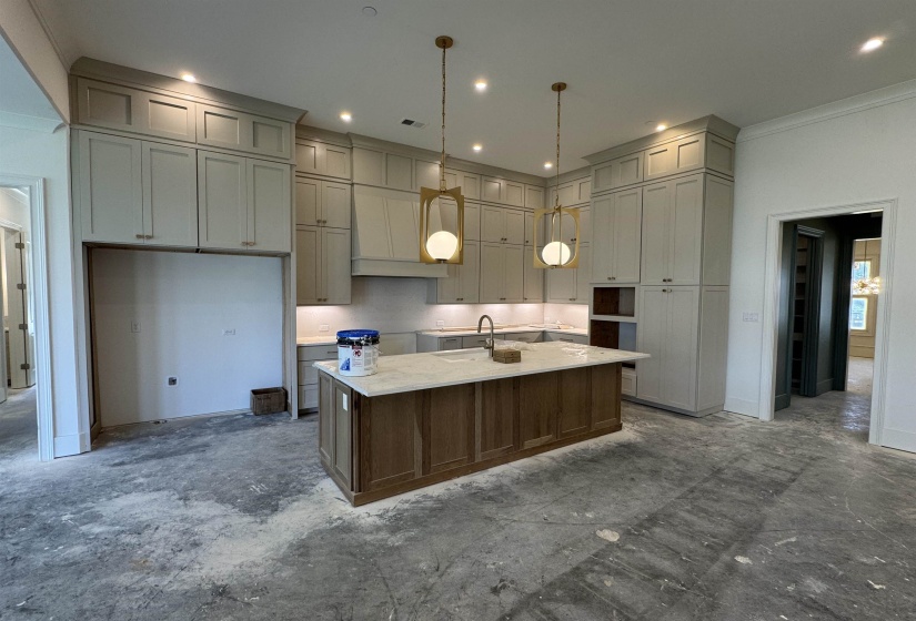 Kitchen featuring full-height cabinetry with crown molding, a central island with paneling, pendant lighting, under-cabinet lighting, and a built-in sink