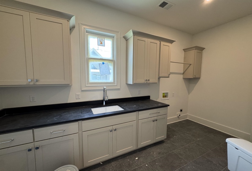 Built-in cabinetry with ample storage, dark countertop with an undermount sink, window with trim, and tile flooring