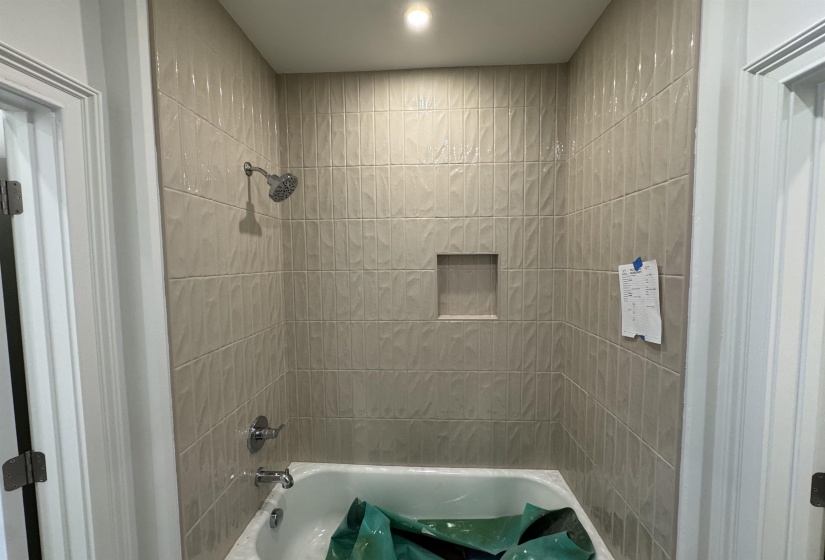 Contemporary bathtub-shower combination with light-toned rectangular wall tiles, an integrated shower niche, and a chrome showerhead with matching fixtures