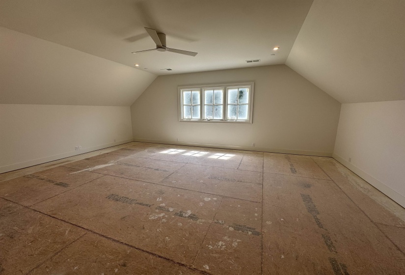 Spacious room featuring sloped ceilings, a multi-pane window, recessed lighting, a ceiling fan, and unfinished subflooring