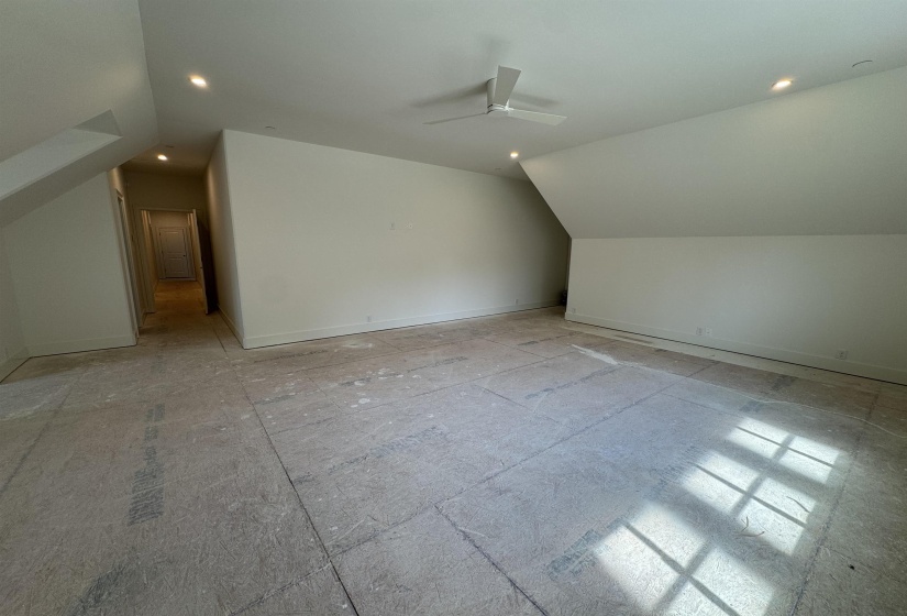 Spacious room featuring sloped ceilings, recessed lighting, and a contemporary ceiling fan