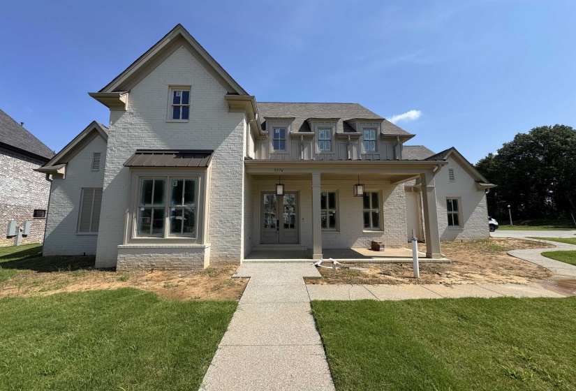 Contemporary brick residence with a covered porch featuring square columns, a dark metal roof accent, and dormer windows